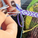 A person weaves a bracelet from purple and white string