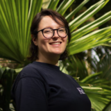 A person in a black sweater and glasses poses for a photo in a tropical space