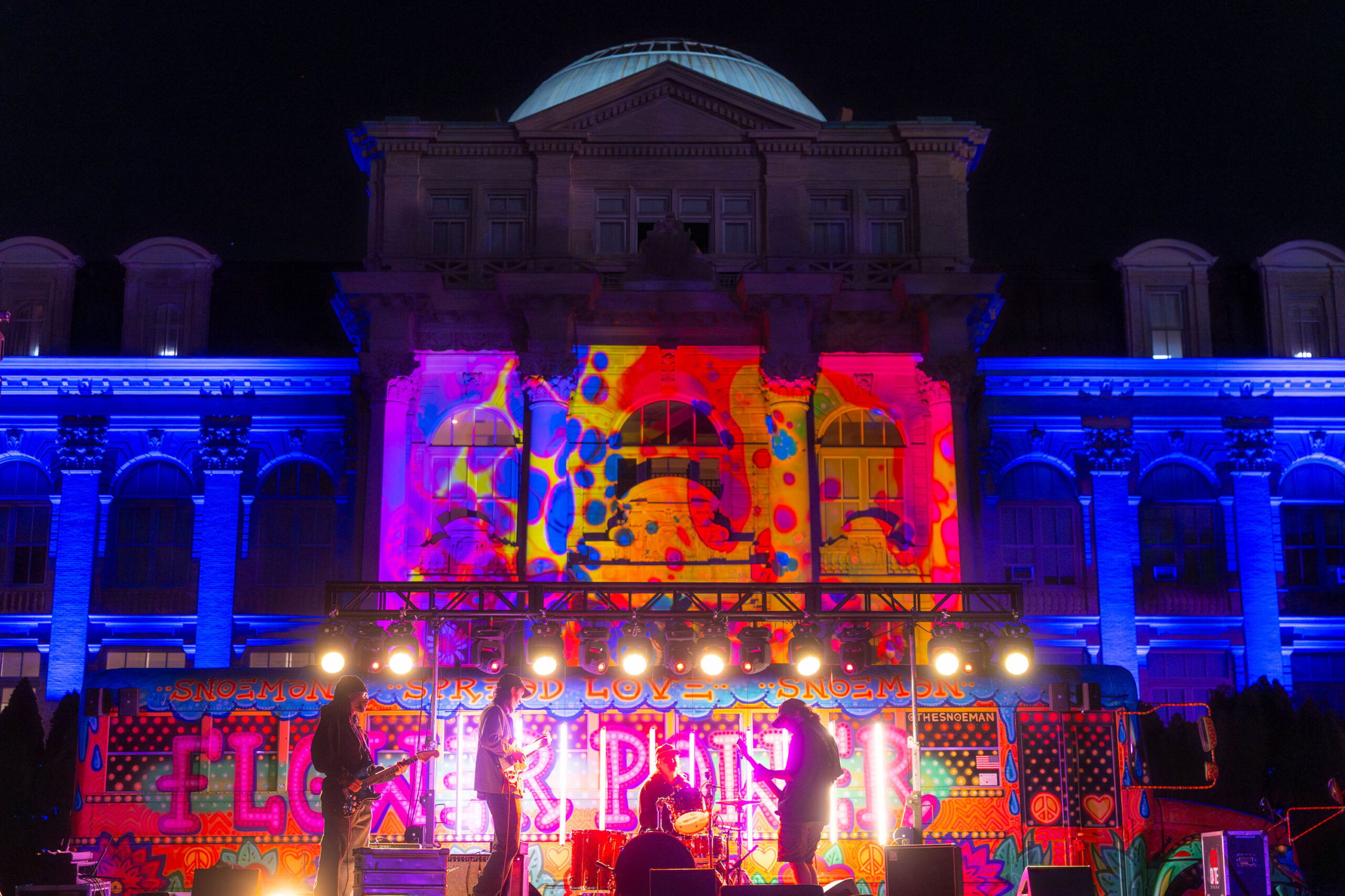 A band plays on a colorfully lit stage beneath the front facade of a large, domed building