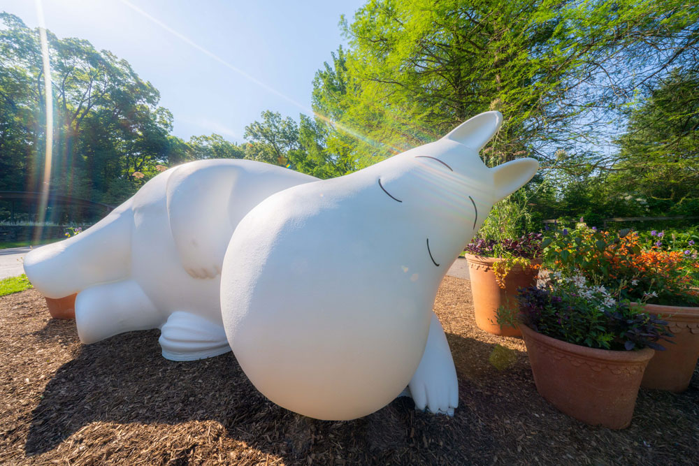 A large white creature statue takes a sleepy pose under the sun