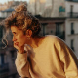 A person in a cream-colored sweater poses for a photo at sunset