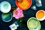 a photograph of an orchid in a small bowl surrounded by other colorful bowls and two perfume bottles