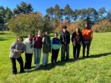 A group of eight young people pose together for a photo on a sunny green lawn
