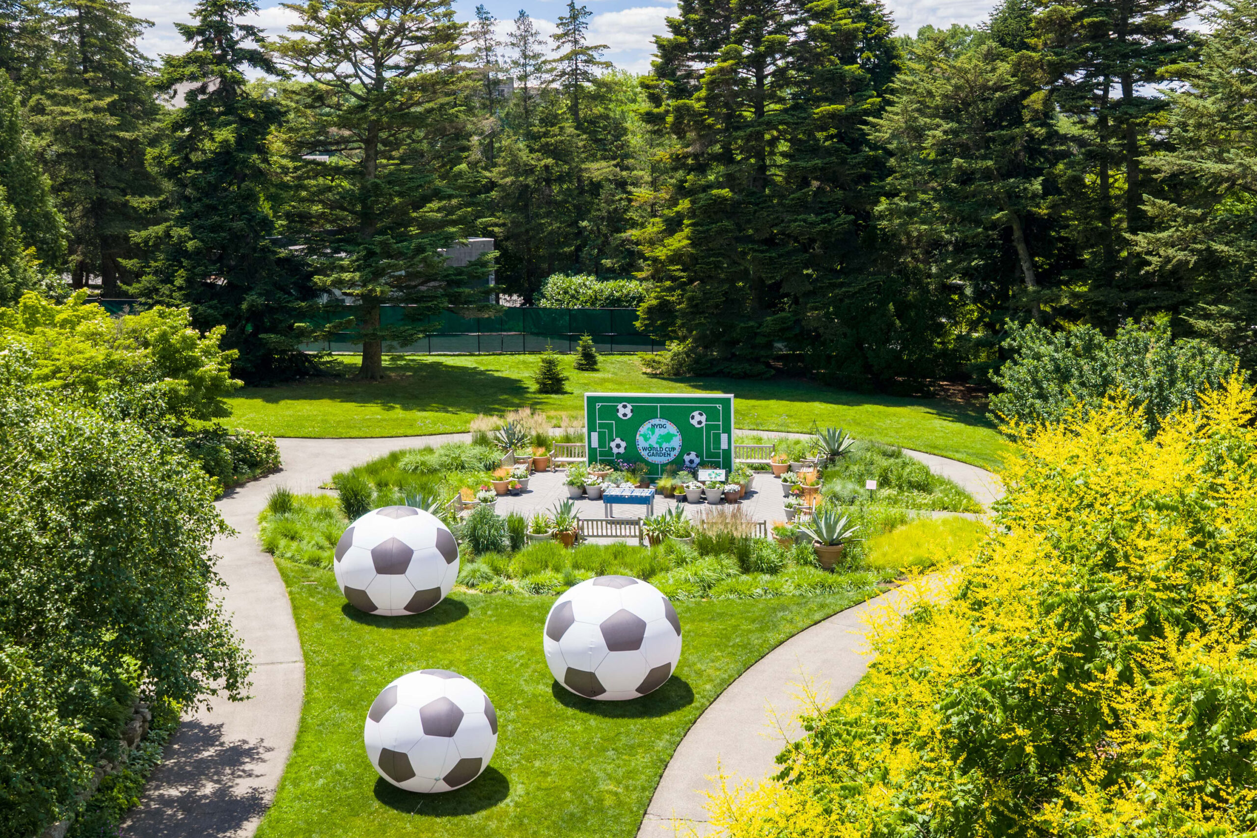 An aerial view of a sunny garden featuring three enormous inflatable soccer balls