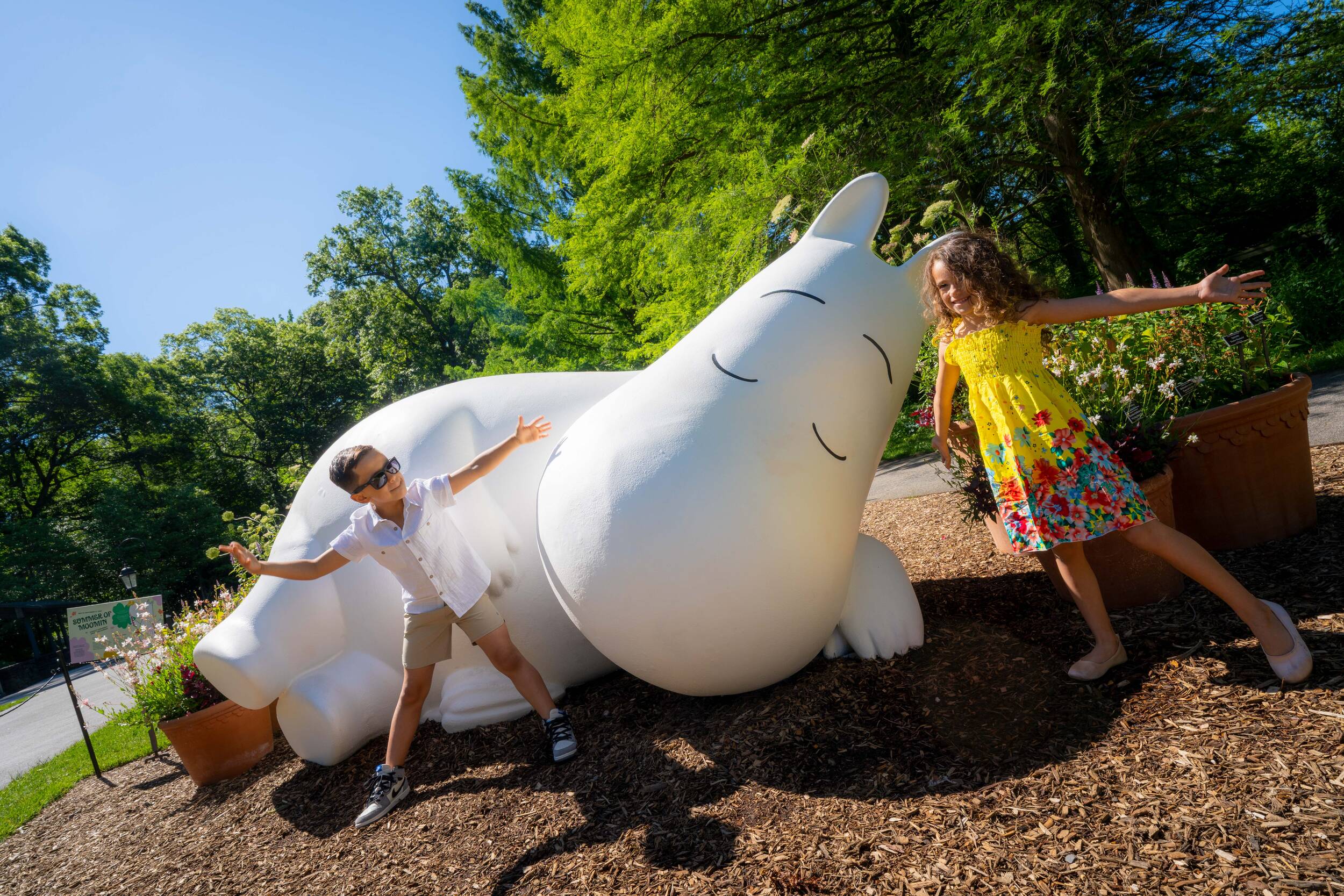 Two children in summer clothes pose for a photo with a large white creature statue