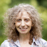 A person with curly gray hair poses for a photo outdoors