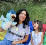An adult and child sing along with a blue bird puppet