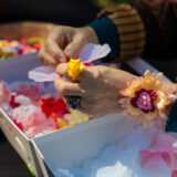 A person creates silk flowers from colorful individual petals arranged in separate boxes