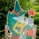 A graphic print of a cartoon character wearing a pointy green hat and yellow shirt, holding fruit as it sits among leaves and flowers