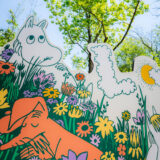 An illustration of a Moomin character and a small orange animal sitting among wildflowers