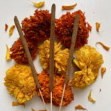 An arrangement of orange and red flowers and brown incense sticks
