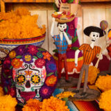 A table covered in orange chrysanthemum flowers, sculptures of skeletons, and a patch featuring a skull