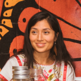 A person wearing a white and red dress, with long dark hair, is photographed in front of a wall depicting black and orange butterfly wings