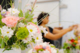 A bouquet of daisies, pink roses, and foliage with a person in the background