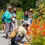 A group of people in colorful summer clothes participate in a class among colorful flowers