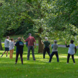A group of people in light fall clothes perform exercises together on a sunny green lawn