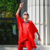 A person in a red outfit and sunglasses dances while pointing to the sky