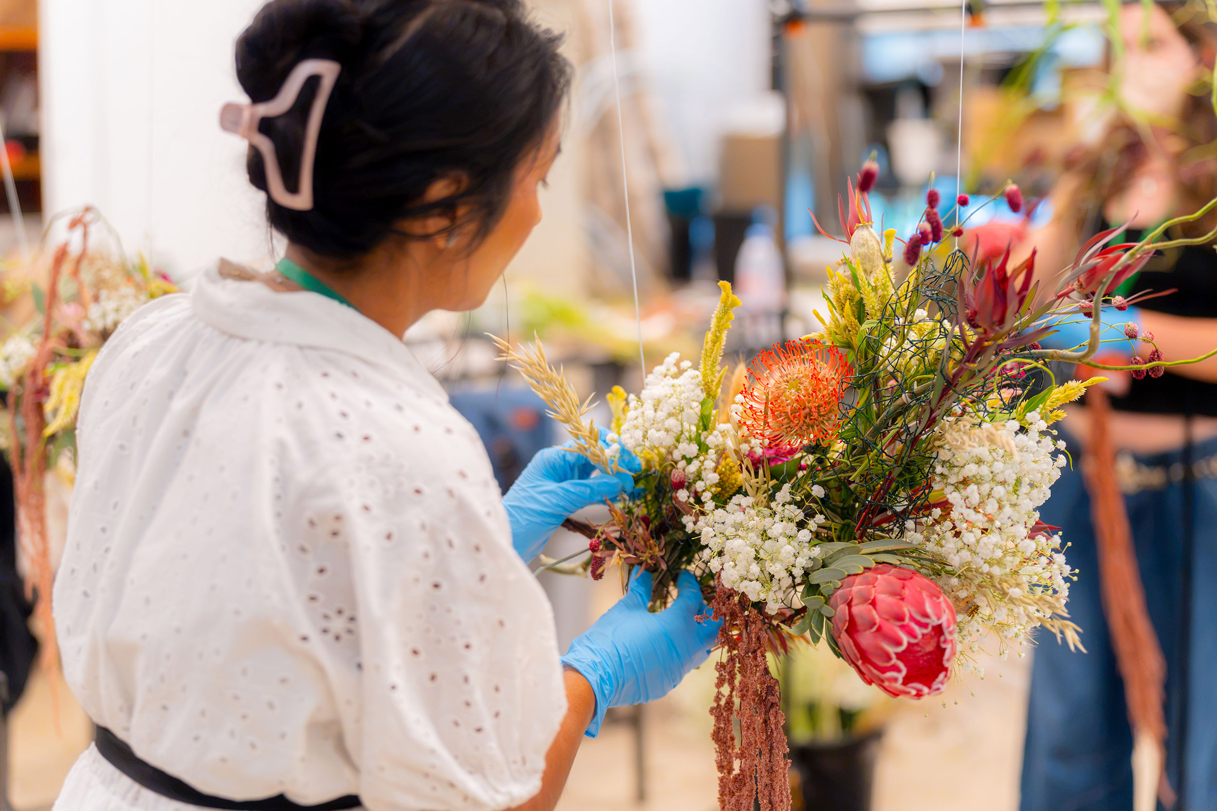 A person arranges flowers in a bouquet with white, pink, and orange flowers