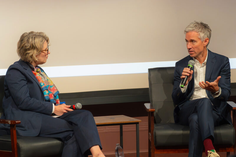 Two people with microphones lead a discussion from a stage