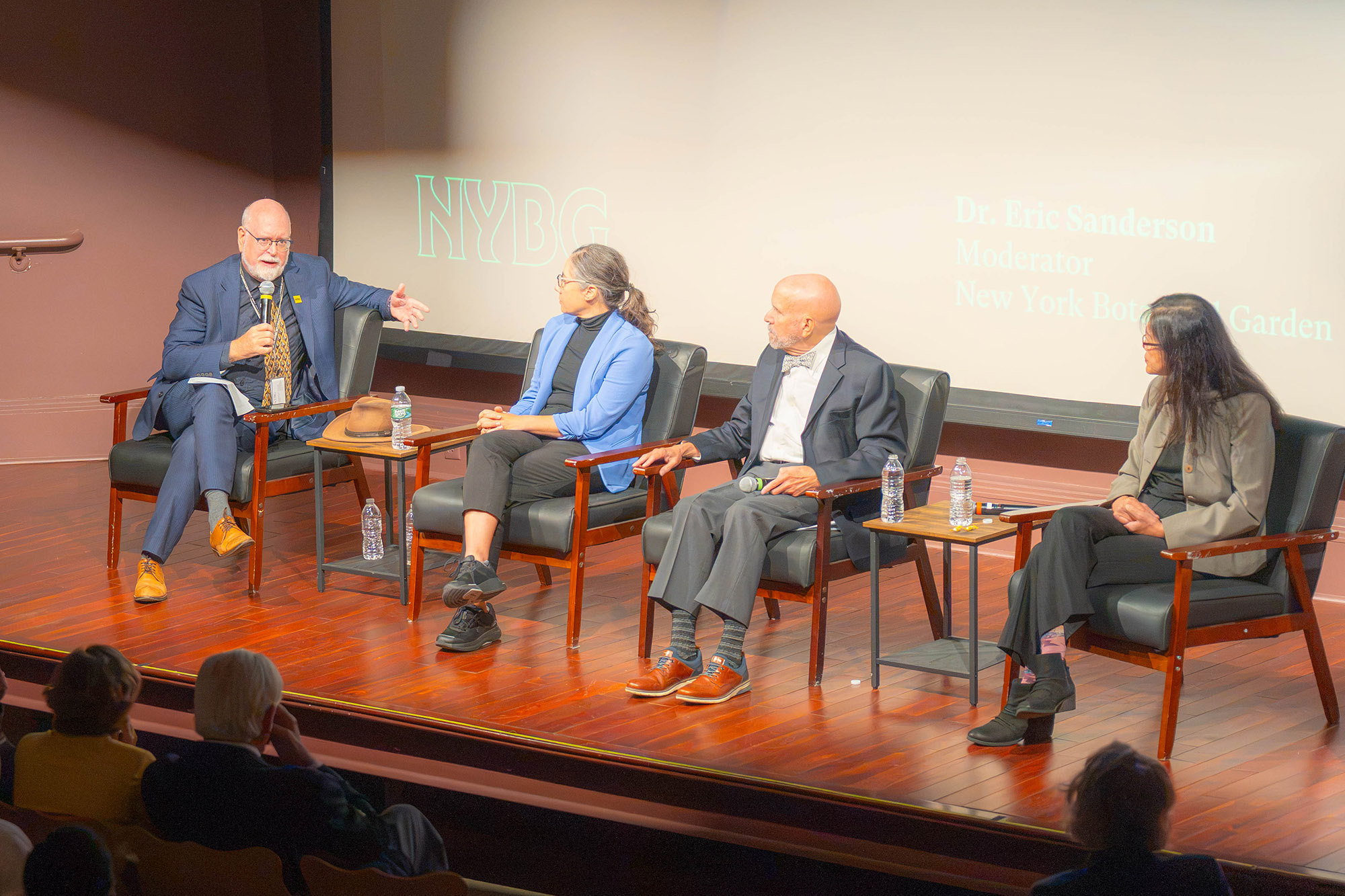 Four people sit in chairs on a lit stage for a panel discussion
