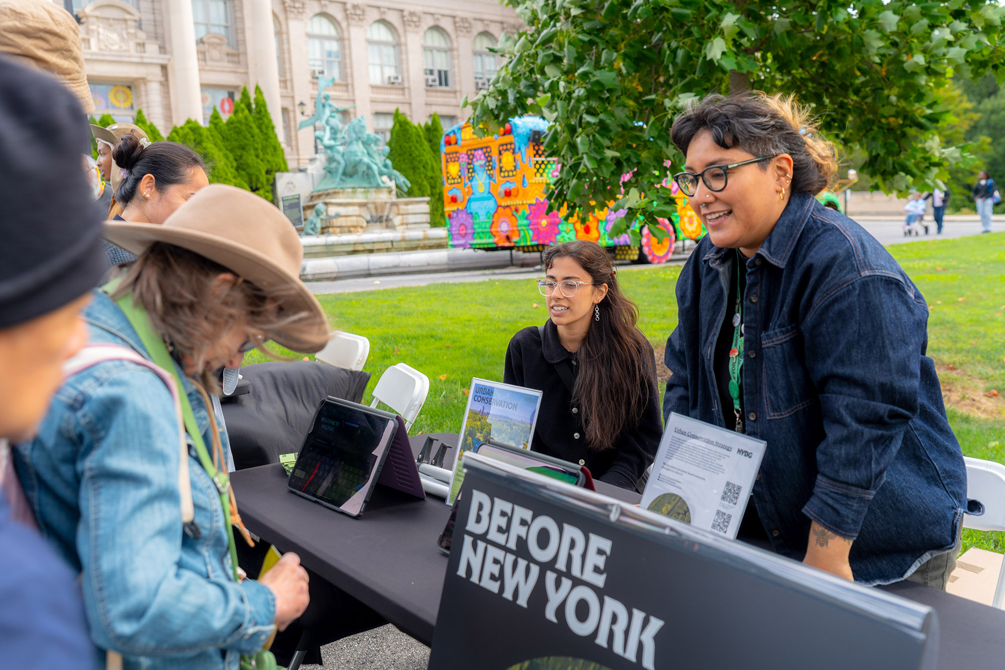 Two people share information with visitors to their outdoor information booth