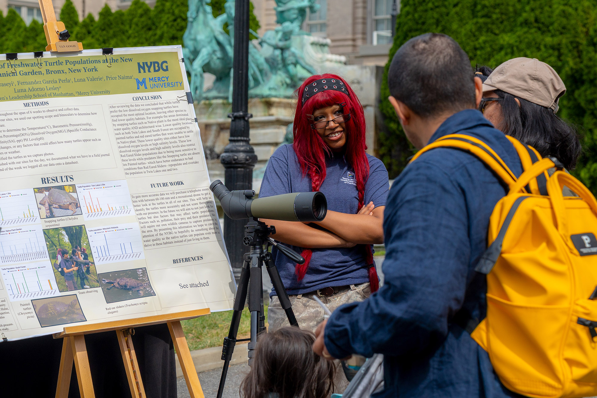 A teenager with red hair discusses a poster board of research findings with a family of three