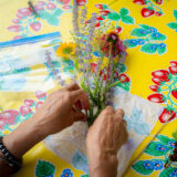 A pair of hands tie together a bouquet of wildflowers on a colorful yellow tablecloth