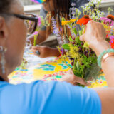 A person in glasses and a blue shirt prepares a colorful bouquet of wildflowers