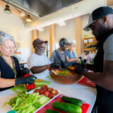 A group of people gather around a kitchen counter to prepare vegetables