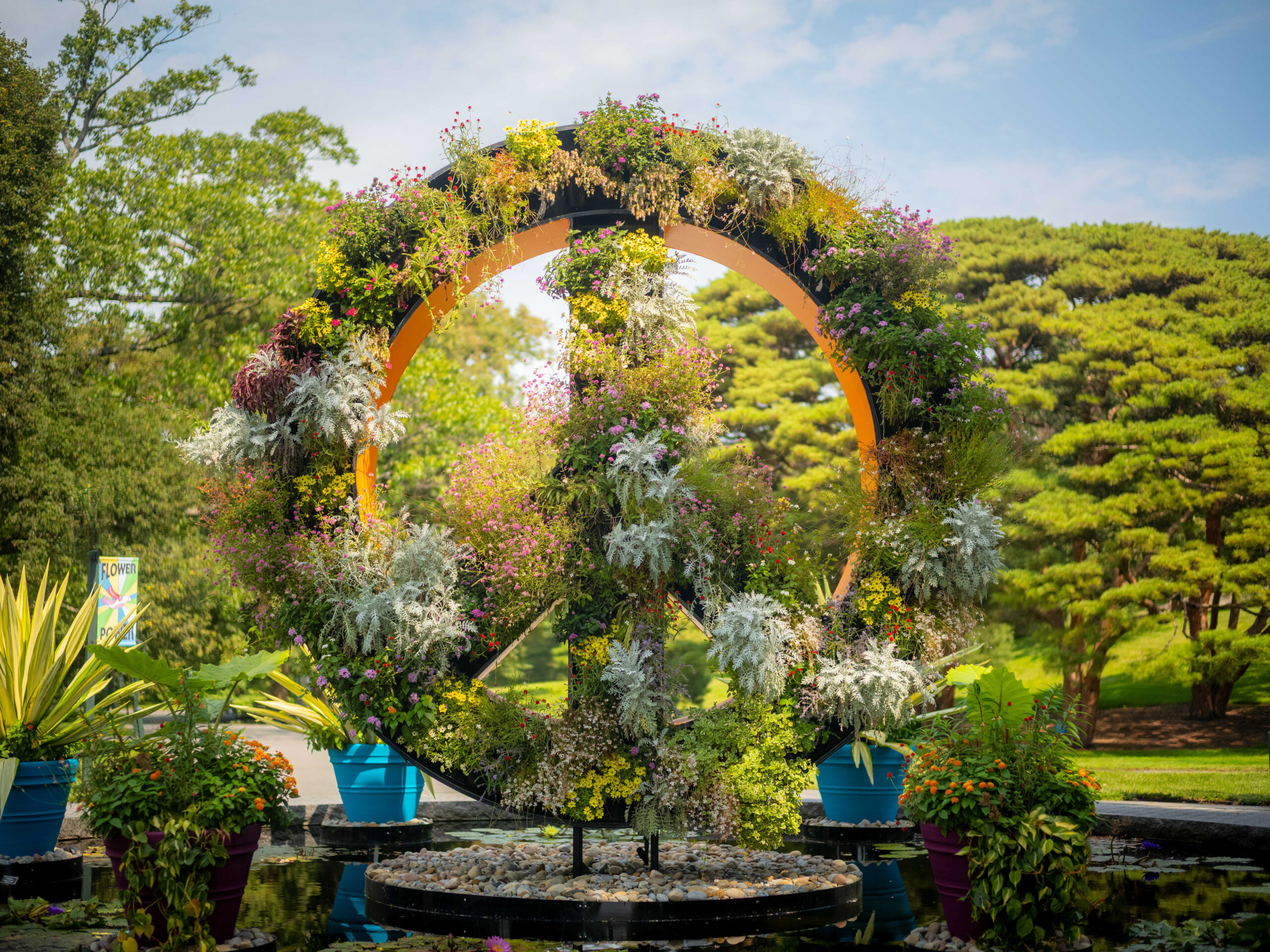 An enormous sculptural peace sign full of bushy plants, outside on a sunny day