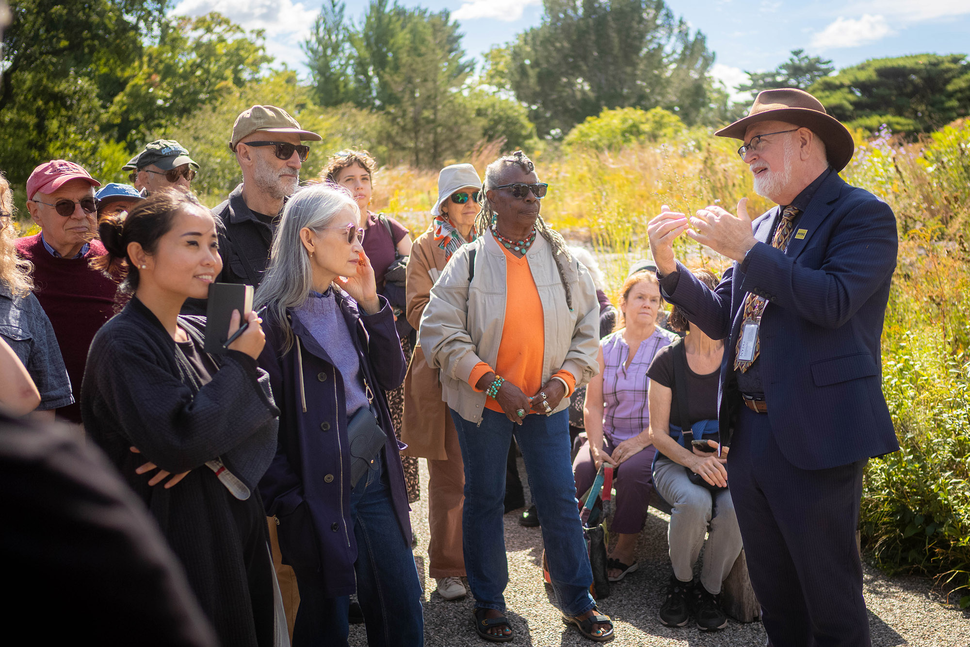 A group of people gather around a tour guide in a sunny outdoor garden space