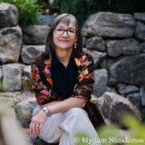 A person in a black shirt and white pants sits along a stone wall