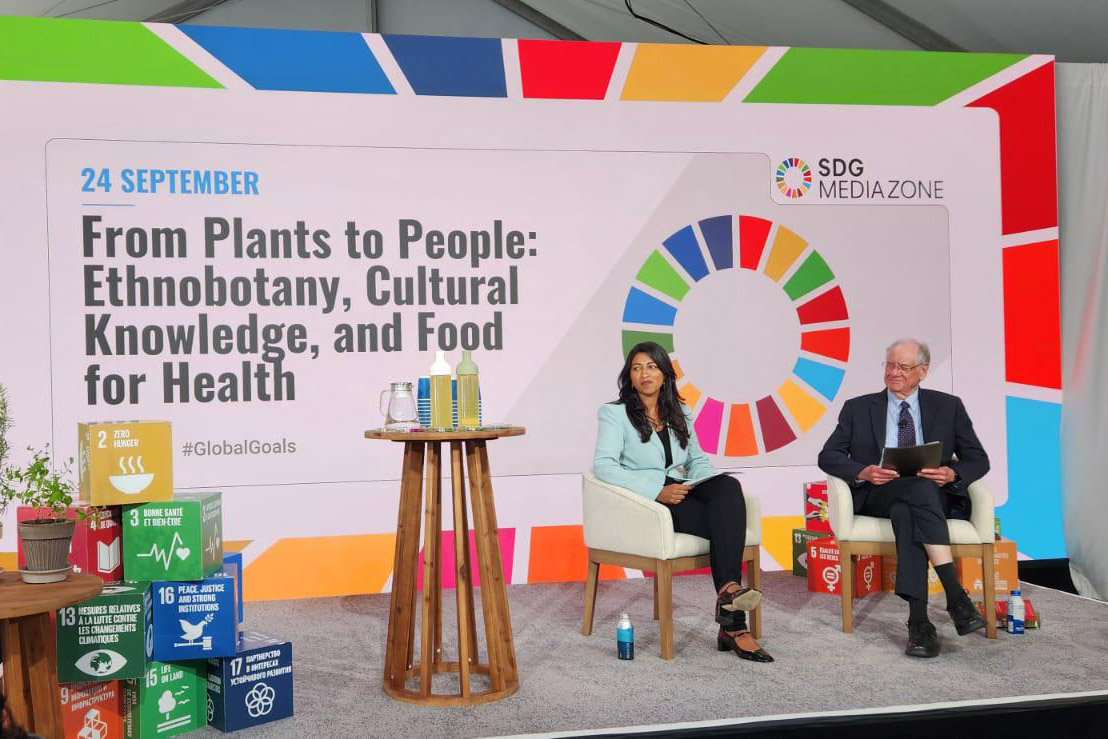 Two people sit on a colorful stage in front of the words 