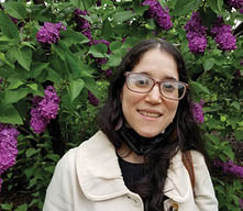 Headshot of Carmen Espinal standing in front of a backdrop of green leaves and purple flowers