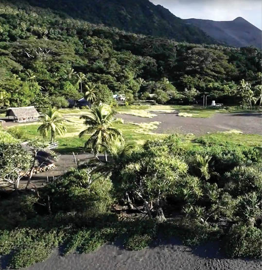 A top-down photo of a small village framed by Brazil s Amazon Rain Forest, with tall mountains far off in the background and palm trees in the foreground